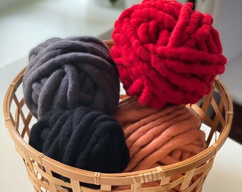 May include: A wicker basket filled with four balls of yarn in different colors: red, gray, black, and peach. The yarn is soft and fluffy, perfect for knitting or crocheting.
