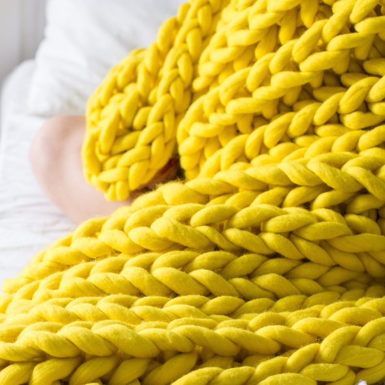 May include: A close-up of a yellow chunky knit blanket. The blanket is made of thick yarn and has a soft, fuzzy texture.