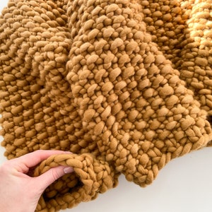 Close-up of beige chunky knit sweater sleeve with thick handspun merino wool stitches.