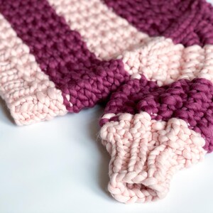 Close-up of burgundy and pale pink sweater sleeves showing the chunky knit texture, striped color placement and ribbed cuffs.