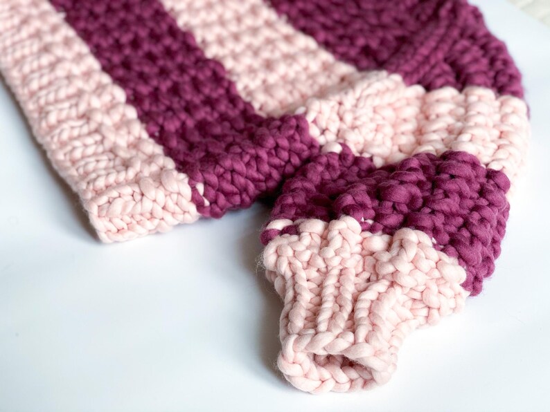 Close-up of burgundy and pale pink sweater sleeves showing the chunky knit texture, striped color placement and ribbed cuffs.