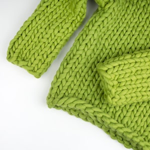 May include: A close-up of a green knitted throw blanket with a chunky knit texture.