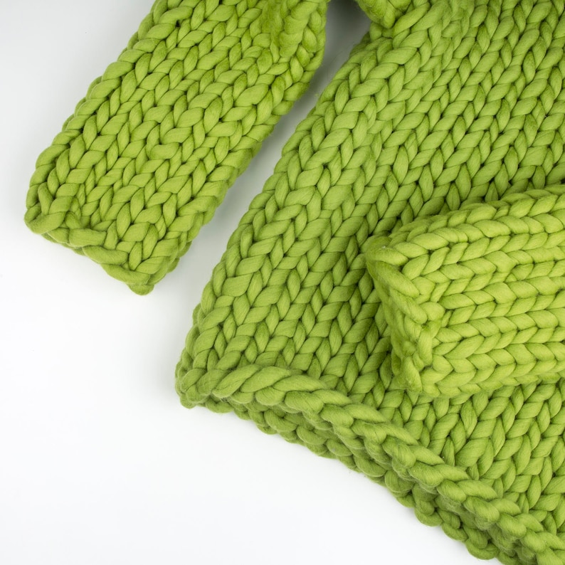 May include: A close-up of a green knitted throw blanket with a chunky knit texture.