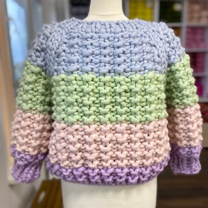 Front view of the pastel striped sweater on a dress form, showing the round ribbed neck, cropped shape and chunky hand-knit texture.