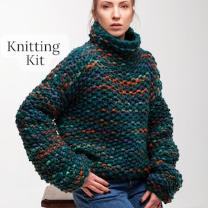 May include: Knitting Kit. A teal, orange, and blue chunky knit turtleneck sweater.