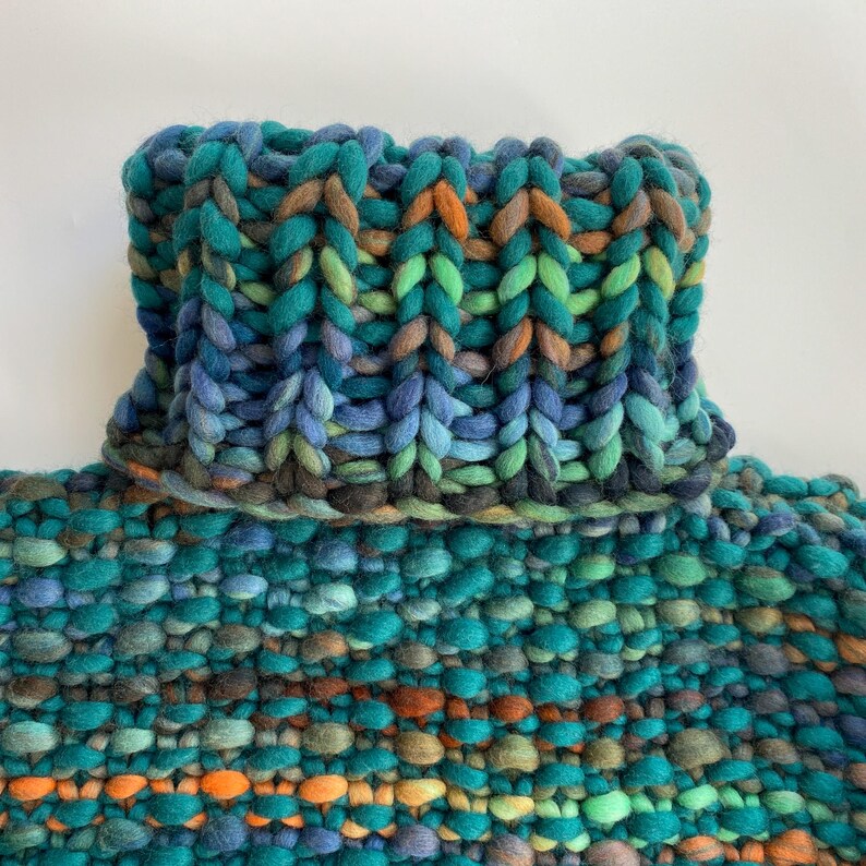 Folded ribbed turtleneck option on green melange chunky knit sweater.