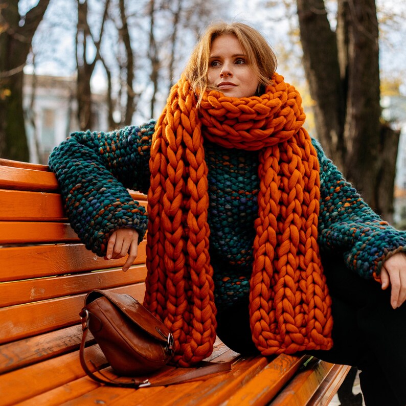 Green melange chunky knit sweater styled with orange oversized scarf for winter outfit inspiration.