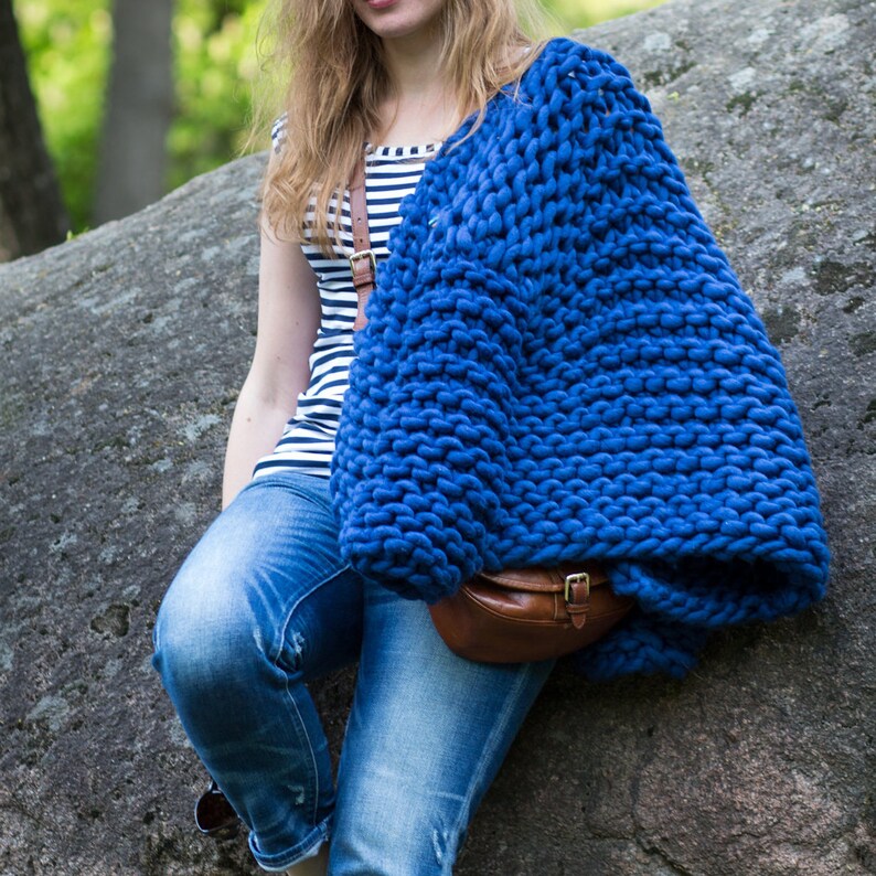 May include: A woman wearing a blue chunky knit cardigan with a brown leather bag. She is wearing a striped shirt and blue jeans.