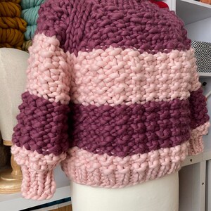 Color block sweater on a dress form, knitted in burgundy and pale pink stripes with three-quarter sleeves and ribbed edges.