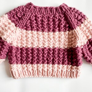 Flat lay of the burgundy and pale pink color block sweater, showing its cropped shape, raglan sleeves and wide striped sections.