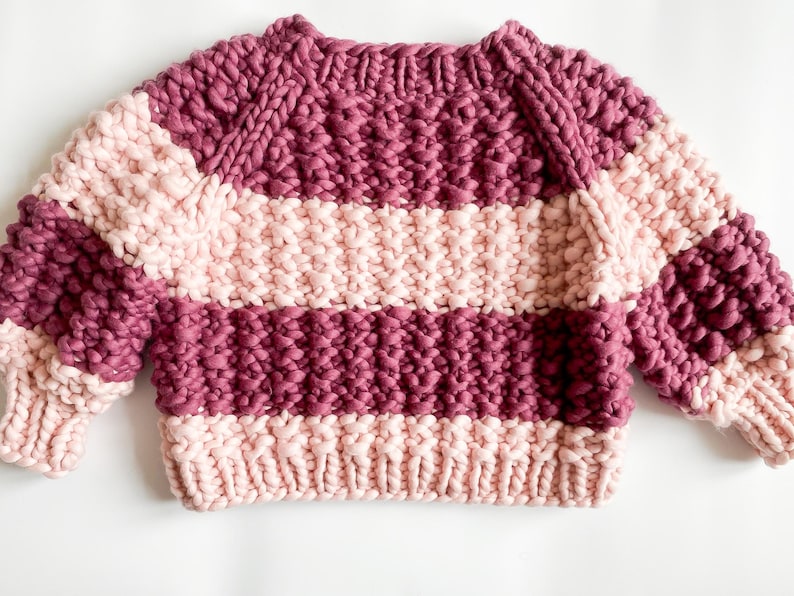 Flat lay of the burgundy and pale pink color block sweater, showing its cropped shape, raglan sleeves and wide striped sections.