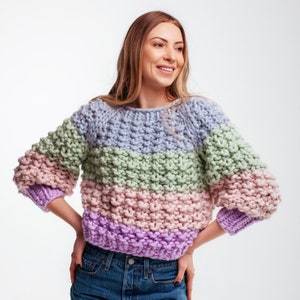 Front view of a cropped knit sweater with blue, green, pink and purple stripes, chunky moss stitch texture and relaxed three-quarter sleeves.