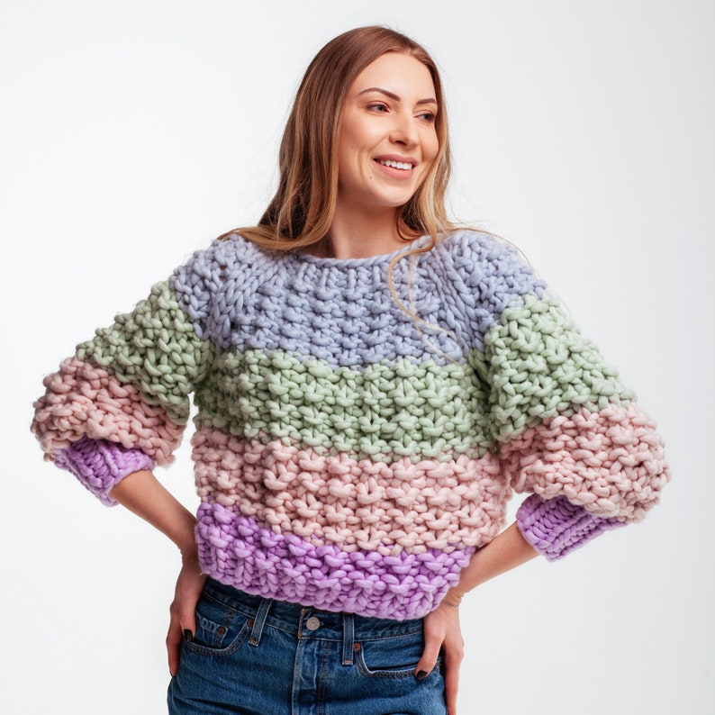 Front view of a cropped knit sweater with blue, green, pink and purple stripes, chunky moss stitch texture and relaxed three-quarter sleeves.