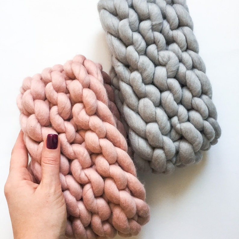 May include: Two chunky knit blankets, one in a light pink color and one in a light gray color. The blankets are made with thick yarn and have a textured, woven look.