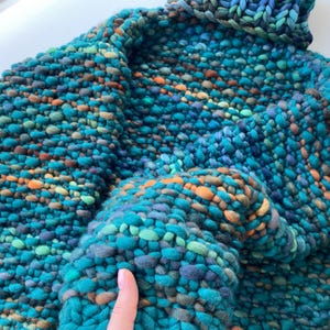 Close-up of green melange sweater sleeve with chunky hand knit merino wool texture.