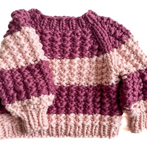 Front flat lay of a burgundy and pale pink striped cropped sweater with raglan sleeves, round ribbed neckline, cuffs and hem.