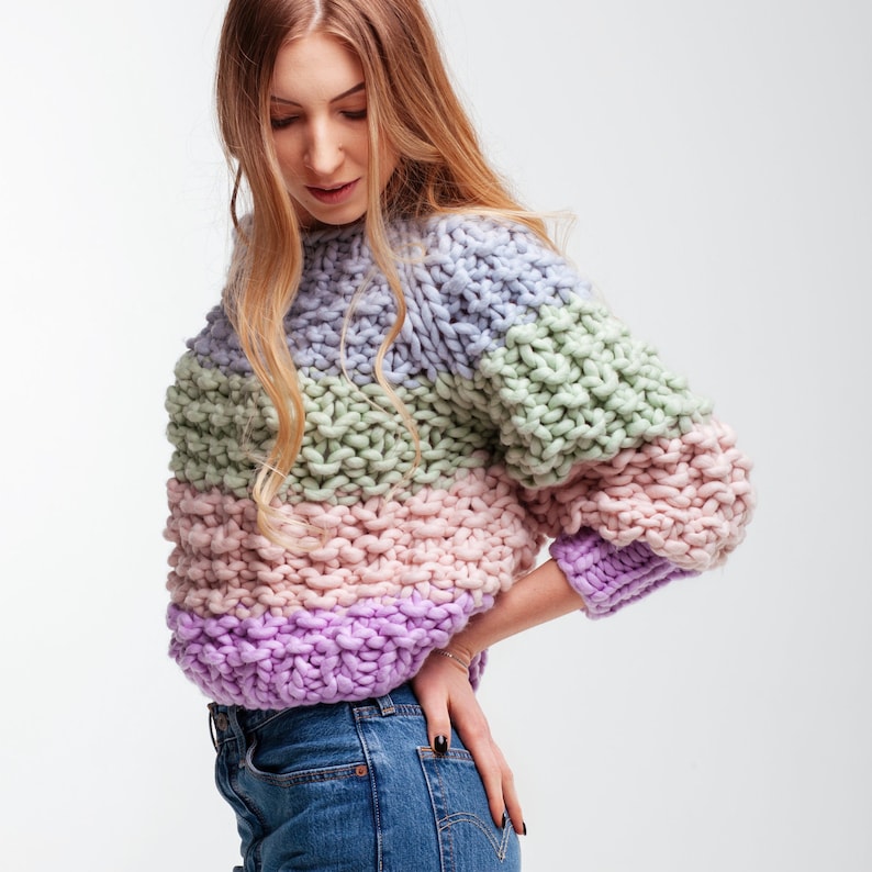 Woman wearing the hand knit merino sweater with a lightly oversized cropped fit, pastel color block stripes and ribbed purple hem and cuffs.