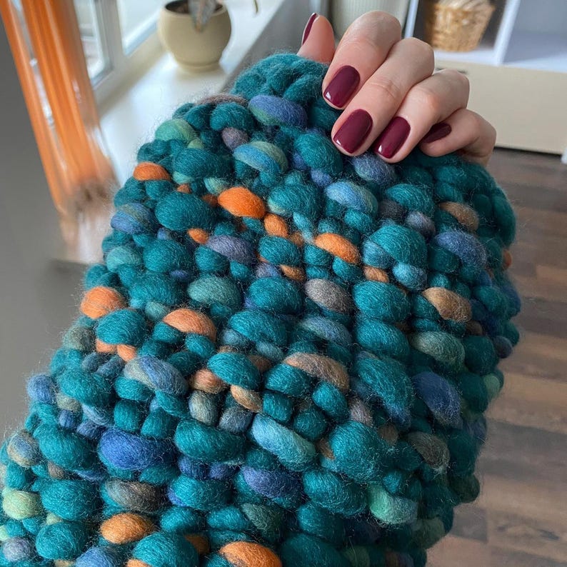 Close-up of hand knit merino wool sweater texture in green, teal and orange melange yarn.