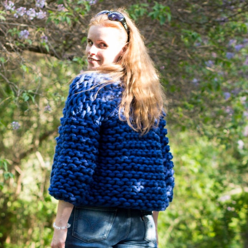 May include: A blue knitted cardigan with a chunky knit texture. The cardigan is cropped and has a relaxed fit.