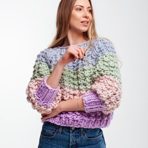 Three-quarter front view of the pastel chunky knit sweater with round neckline, color block stripes and loose three-quarter sleeves.