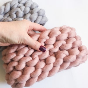 May include: Two chunky knit blankets, one in a light gray color and the other in a dusty rose color. The blankets are made with thick yarn and have a soft, textured look.