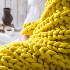 May include: A close-up of a yellow chunky knit blanket. The blanket is made of thick yarn and has a soft, cozy texture.