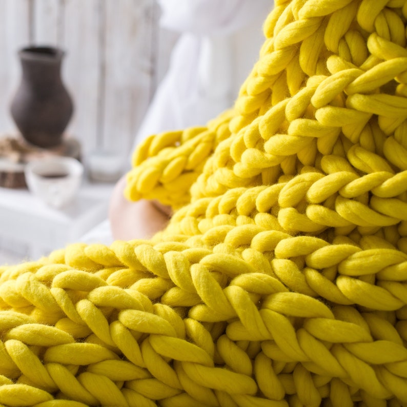 May include: A close-up of a yellow chunky knit blanket. The blanket is made of thick yarn and has a soft, cozy texture.