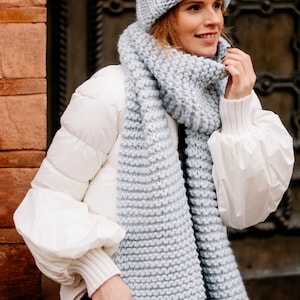 Peut inclure: Une écharpe et un bonnet en tricot bleu clair assortis. L'écharpe est longue et épaisse, et le bonnet est ample.