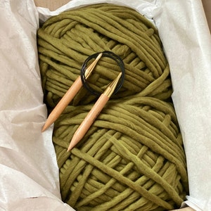 May include: A large skein of olive green yarn with two wooden knitting needles and a black metal ring.