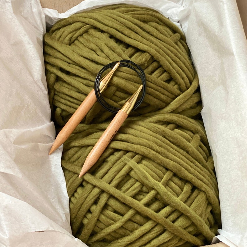 May include: A large skein of olive green yarn with two wooden knitting needles and a black metal ring.