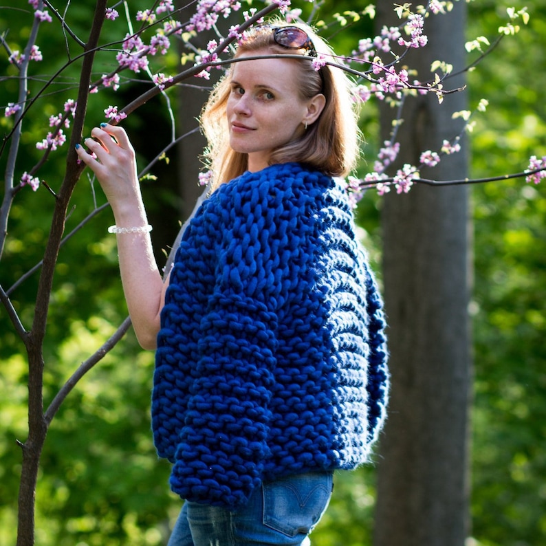 May include: A blue chunky knit cardigan with a relaxed fit. The cardigan is made with a thick yarn and has a simple design.
