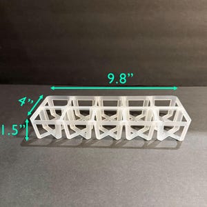 May include: A clear plastic grid with multiple square compartments. The grid is 9.8 inches long, 4 inches wide, and 1.5 inches tall. The design features a series of intersecting lines forming the compartments, suitable for organizing small items.