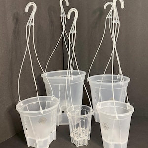 May include: A collection of clear plastic hanging plant pots in various sizes. Each pot has a white plastic hook and hanging wires. The pots are designed with drainage holes and a textured surface. The background is a dark gray.