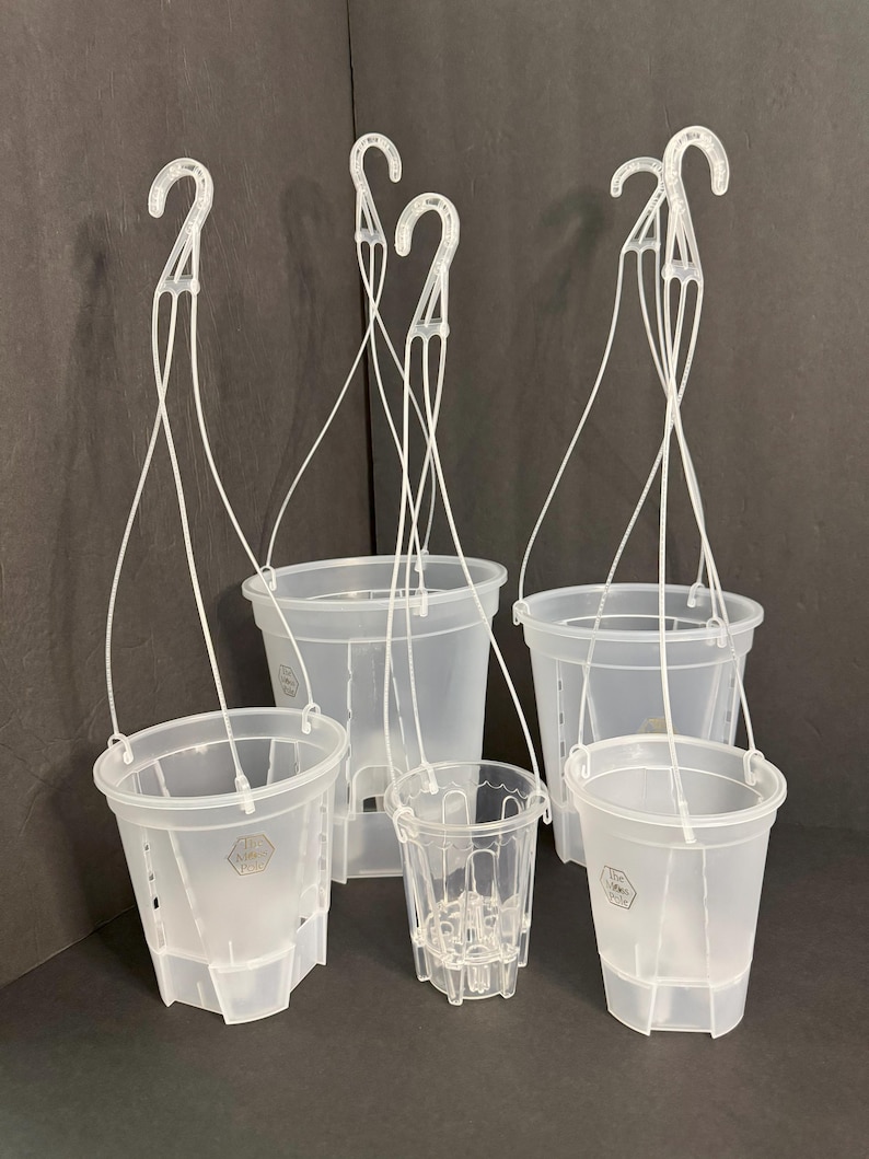 May include: A collection of clear plastic hanging plant pots in various sizes. Each pot has a white plastic hook and hanging wires. The pots are designed with drainage holes and a textured surface. The background is a dark gray.