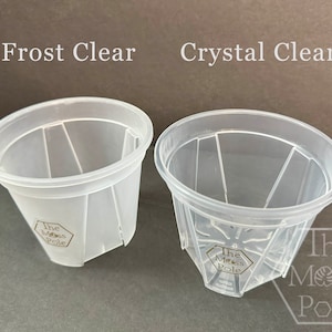 Peut inclure: Deux pots de plantes en plastique transparent, l'un avec une finition givr&eacute;e et l'autre avec une finition transparente. Les deux pots ont un logo hexagonal qui indique "The Moss Pole".
