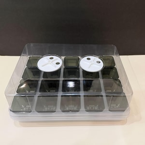 May include: A clear plastic seed starting tray with a clear lid. The tray has 15 individual cells with dark green lids. Two white, circular vents are on top of the lid.