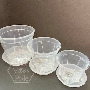 Peut inclure: Trois pots de fleurs en plastique transparent avec des trous de drainage et des soucoupes assorties. Les pots sont embo&icirc;t&eacute;s les uns dans les autres, le plus grand en bas et le plus petit en haut. Les pots ont un design hexagonal et le texte "The Moss Pole" est imprim&eacute; au fond de chaque pot.