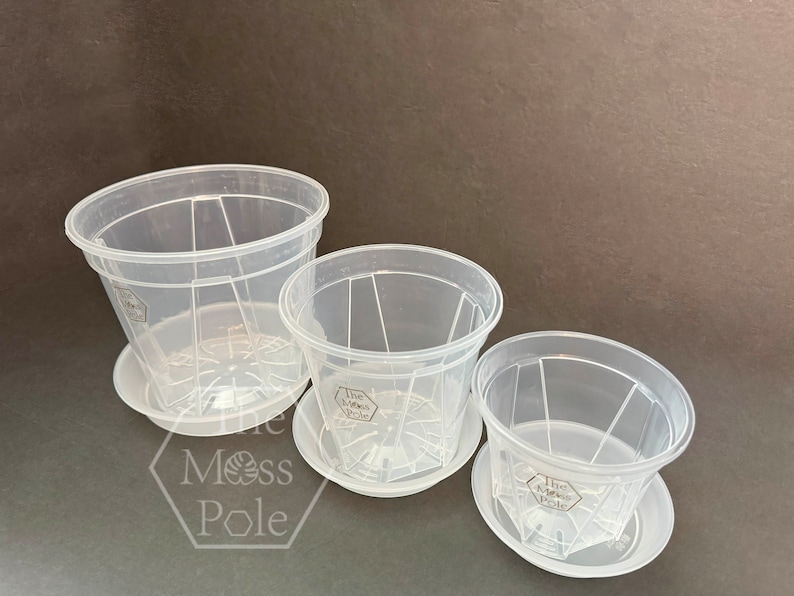 Peut inclure: Trois pots de fleurs en plastique transparent avec des trous de drainage et des soucoupes assorties. Les pots sont embo&icirc;t&eacute;s les uns dans les autres, le plus grand en bas et le plus petit en haut. Les pots ont un design hexagonal et le texte "The Moss Pole" est imprim&eacute; au fond de chaque pot.