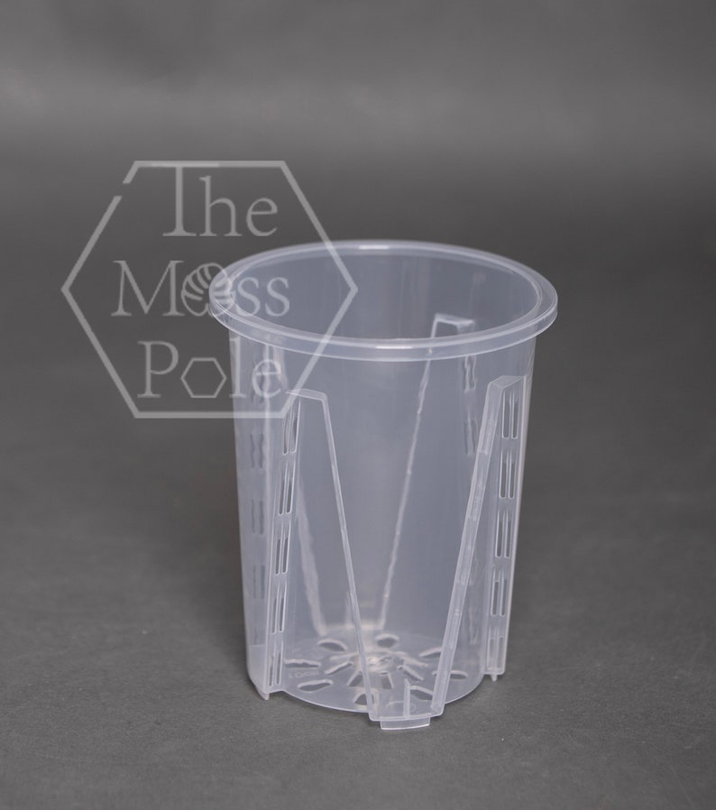 May include: A clear plastic plant pot with drainage holes and a grid pattern around the sides. The pot is designed for use with hydroponic systems.