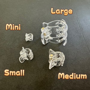 May include: Four clear plastic hair clips in different sizes: mini, small, medium, and large. The clips are all the same design, with a curved shape and a small gold metal piece in the center.