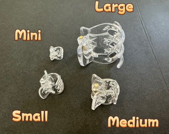 Peut inclure: Quatre pinces à cheveux en plastique transparent de différentes tailles : mini, petite, moyenne et grande. Les pinces sont toutes du même design, avec une forme incurvée et une petite pièce en métal doré au centre.