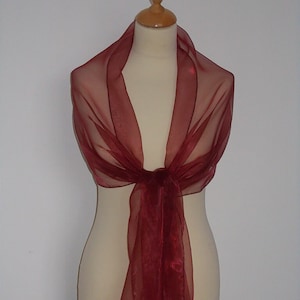 May include: A burgundy sheer shawl made of soft, lightweight fabric. The shawl is draped over a mannequin and tied at the neck.