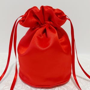 May include: A bright red satin drawstring bag with a gathered top and long ties. The bag is ideal for holding small items such as jewellery or gifts.