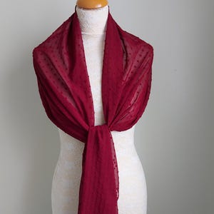 Peut inclure: Une écharpe en mousseline rouge bordeaux à motif de pois. L'écharpe est drapé autour d'un mannequin blanc.