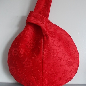 May include: A red fabric bag with a floral pattern. The bag is made in a knot shape and has a single strap.