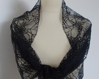 May include: Black lace scarf with a spiderweb pattern. The scarf is draped over a mannequin's shoulders.