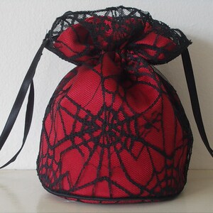 May include: A red drawstring bag with black lace trim and a spiderweb design. The bag has two black ribbon ties.