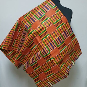 Pode incluir: Um tecido vibrante e estampado drapeado sobre um manequim. O tecido apresenta um design geométrico repetitivo em tons de laranja, verde, azul e amarelo. O tecido é provavelmente usado para roupas ou decoração de casa.