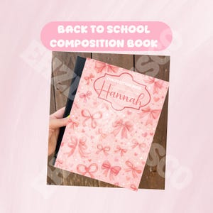 May include: A composition book with a light pink cover featuring a repeating pattern of pink bows and small hearts. The center of the cover displays a decorative frame containing the text "COMPOSITION BOOK" and the name "Hannah" in script.