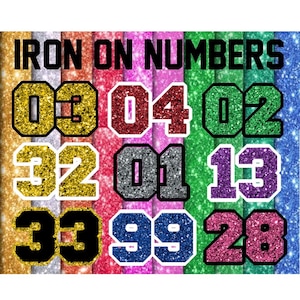 May include: A collection of iron-on numbers in various colors, including gold, red, green, silver, purple, pink, and blue. Each number has a glittery texture and a contrasting outline. The text "IRON ON NUMBERS" is displayed at the top.